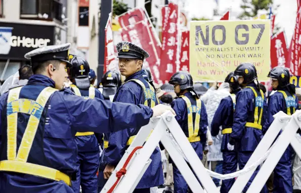  ?? PHOTO: REUTERS ?? Conflict and peace . . . Police officers stand guard as Japanese activists protest against the G7 summit near the Peace Memorial Park, in Hiroshima yesterday.