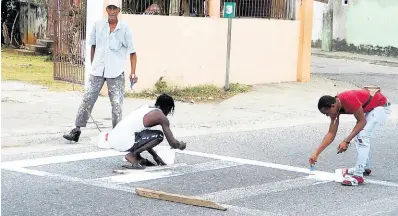  ?? PHOTO BY CARL GILCHRIST ?? These men repaint a pedestrian crossing in Oracabessa, St Mary, frequently used by students of both Oracabessa High and Primary schools.