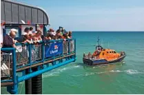  ??  ?? A small crowd clusters outside the lifeboat station to watch a Tamar-class boat set off from the pier (above).