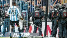  ?? Foto: nordphoto ?? Der 1860 Spieler Abdoulaye Ba trägt eine Stange vom Platz, die von aufgebrach­ten Fans auf das Spielfeld geworfen wurde. Die Polizei versucht derweil, die wütende Menge in der Nordkurve in Schach zu halten.