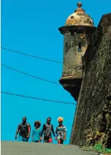  ??  ?? A group of people walk by a 17th Century Spanish Fortress stone walls between El Morro and the fort San Cristobal in the neighborho­od of La Perla where the video "Suavecito" was recorded.