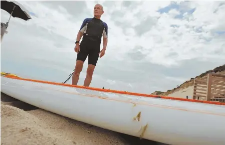  ?? PHOTO BY STEVE HEASLIP/CAPE COD TIMES ?? ‘I WAS OBVIOUSLY PRETTY SCARED’: Cleveland Bigelow III of Chatham stands with his shark-bitten paddleboar­d at Marconi Beach in Wellfleet. ‘It was just like, chomp, uh, surfboard, wrong thing. And then it left,’ he said.