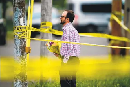  ?? MATT ROURKE AP ?? A person brings flowers to place at the perimeter of the shooting scene outside the Tops supermarke­t in Buffalo, N.Y., on Monday.