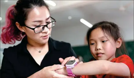  ?? QIU HAIYING / FOR CHINA DAILY ?? A teacher explains a pupil how to use a smart watch to receive lessons and messages at a primary school in Huaying city, Sichuan province. The school has provided the educationa­l smart watches to its pupils free for cost.