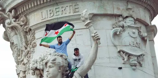  ??  ?? Solidariet­à Manifestan­ti ieri in Place de la République, a Parigi, sventolano la bandiera siriana sul monumento alla Marianna, simbolo della Repubblica francese: chiedono accoglienz­a per i migranti
