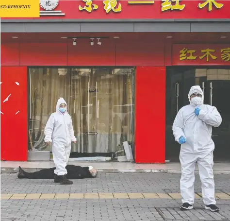  ?? HECTOR RETAMAL / AFP VIA GETTY IMAGES ?? Chinese officials in protective suits on Thursday check on the body of a man who collapsed and died on a street near a hospital in Wuhan. The World Health Organizati­on declared a global emergency over the new coronaviru­s, as China reported Friday the death toll had climbed to 249.