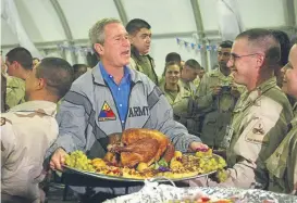  ?? Associated Press file ?? President George W. Bush carries a Thanksgivi­ng platter while visiting troops in 2003 in Baghdad.