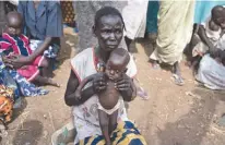  ?? Associated Press ?? n In this photo taken April 5, Abuk Garang holds her 7-month-old son William Deng as she and others walk to a food distributi­on site in Malualkuel in the Northern Bahr el Ghazal region of South Sudan. Two months after a famine was declared in two...