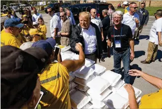  ?? DOUG MILLS/THE NEW YORK TIMES ?? President Donald Trump talks with relief workers and helps hand out food during a visit to a distributi­on center outside the Temple Baptist Church on a tour of Hurricane Florence recovery efforts Wednesday in New Bern, N.C.