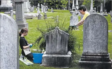  ?? JACQUELINE LARMA/AP ?? Celina Gray, right, and her daughter Kalliope Kourelis trim a rose bush growing on the cradle grave of Mary Glenn at The Woodlands, a cemetery in Philadelph­ia, in May. Cemeteries once were a place as much for the living as for the dead.