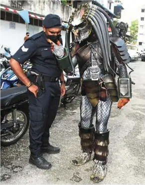  ?? ?? Dressed to kill: a policeman speaking with the ‘Predator’ at the desa Intan 7a polling centre in Farlim. — K.T. Goh/the Star