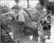  ?? ASSOCIATED PRESS ?? IN THIS JAN. 1, 1966, FILE PHOTO, a Paratroope­r of the 173rd U.S. Airborne brigade crouches with women and children in a muddy canal as intense Viet Cong sniper fire temporaril­y pins down his unit during the Vietnamese War near Bao trai in Vietnam....