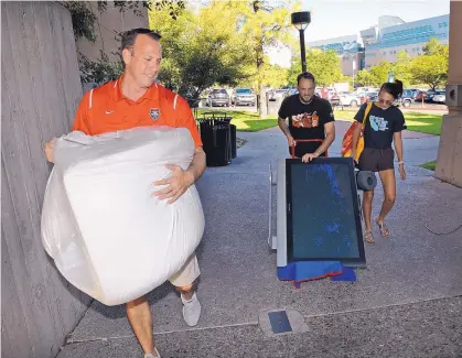  ?? JIM THOMPSON/JOURNAL ?? UNM Athletic Director Eddie Nuñez carries a bag of stuff into DeVargas Hall for Samantha Lambrecht as she moved in. Also helping move a TV is her father, Michael Lambrecht.