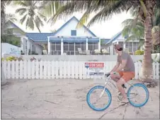  ?? MOISES CASTILLO/ ASSOCIATED PRESS ?? A man rides a bike past the entrance to John McAfee’s home in Ambergris Caye, Belize. McAfee has been identified as a " person of interest" in the killing of his neighbor, Gregory Viant Faull.