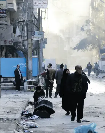  ?? LOUAI BESHARA / AFP / GETTY IMAGES ?? Syrians walk past destroyed buildings in Aleppo’s al-Shaar neighbourh­ood on the weekend, a month after government forces retook the Syrian city from rebel fighters.