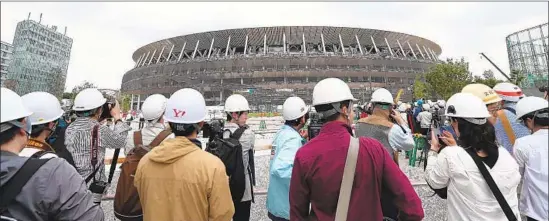  ?? Behrouz Mehri AFP/Getty Images ?? MEDIA MEMBERS visit the constructi­on site of the new National Stadium, whose original, $2-billion design was scrapped and replaced by one about half the price.