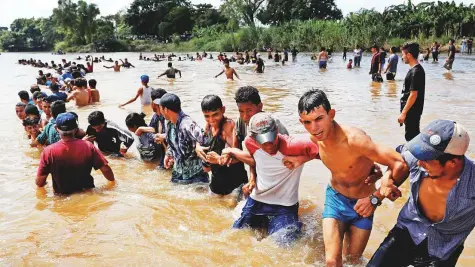  ?? Reuters ?? Migrants, part of a caravan travelling to the United States, make a human chain to pull people from the river between Guatemala to Mexico in Ciudad Hidalgo and continuing to walk in Mexico on Monday.