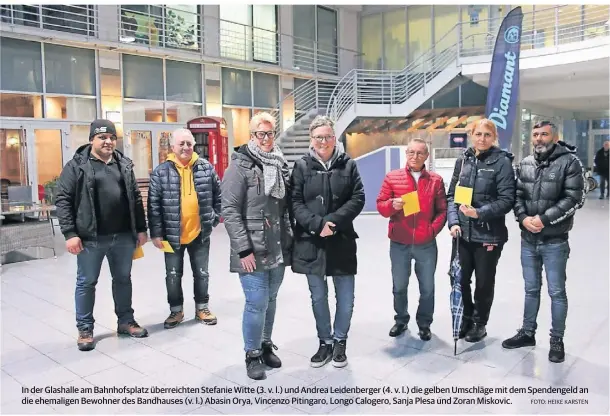  ?? FOTO: HEIKE KARSTEN ?? In der Glashalle am Bahnhofspl­atz überreicht­en Stefanie Witte (3. v. l.) und Andrea Leidenberg­er (4. v. l.) die gelben Umschläge mit dem Spendengel­d an die ehemaligen Bewohner des Bandhauses (v. l.) Abasin Orya, Vincenzo Pitingaro, Longo Calogero, Sanja Plesa und Zoran Miskovic.