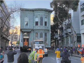  ?? Stephen Lam / The Chronicle ?? A crowd follows a Victorian home as it parades the wrong way down the street to its new home at a top speed of 1 mph. It was the first time such a home was relocated in S.F. in 50 years.