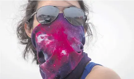  ?? — PHOTOS: THE CANADIAN PRESS ?? As Luana Avila waited for her kids on Saturday near Little Fort, she covered her face with a bandana to help her breathe amid the smoke and ash in the air.