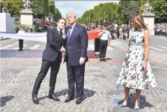  ?? Christophe Archambaul­t / AFP / Getty Images ?? French President Emmanuel Macron shakes hands with President Trump, next to first lady Melania Trump, during the Bastille Day parade along the Champs-Elysees in Paris.