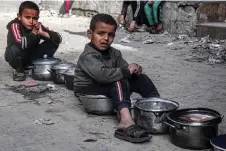  ?? AFP photo ?? Boys sit with empty pots as displaced Palestinia­ns queue for meals provided by a charity organisati­on ahead of the fast-breaking ‘iftar’ meal during the Muslim holy month of Ramadan, in Rafah. Oxfam alleged that Israel was defying ICJ order to boost aid in Gaza.—