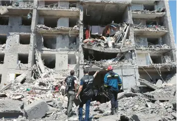  ?? OLEKSANDR GIMANOV/GETTY-AFP ?? A war crimes prosecutor, center, is flanked by members of a civilian rescue crew as they examine a building that was destroyed Friday in the southern Ukrainian town of Serhiivka during a Russian missile strike.