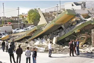  ??  ?? People gather around a leveled building in the town of Darbandikh­an in Iraqi Kurdistan on Monday following a 7.3-magnitude quake that hit the Iraq-Iran border area on Sunday. (AFP)