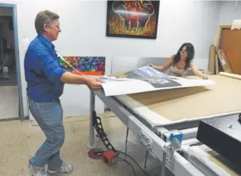  ?? Photos by Andy Cross, The Denver Post ?? Kim Reed, left, president of Reed Art & Imaging, and Shannon Schultz move dye sublimatio­n prints to a heat press. The business is moving to Lakewood.