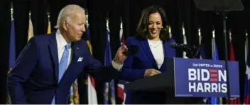  ?? Carolyn Kaster ?? Democratic presidenti­al candidate former Vice President Joe Biden retrieves his face mask from the podium as his running mate Sen. Kamala Harris, D-Calif., prepares to speak at a campaign event at Alexis Dupont High School in Wilmington, Del., Wednesday.