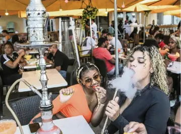  ?? AL DIAZ adiaz@miamiheral­d.com ?? A new law breaks from the lax permit-review system for Miami Beach’s sidewalk cafes, which may place an additional burden on South Beach clubs already bracing for a ban on early-morning alcohol sales. Above, spring breakers Karsyn Mcleod, 21, and Zayasha Fowler, 21, sit at a hookah bar and lounge on Ocean Drive in South Beach on March 12.