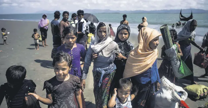  ??  ?? Rohingya Muslim refugees walk on the Bangladesh­i shoreline of the Naf River after crossing the border from Myanmar in Teknaf on Sept. 30.
