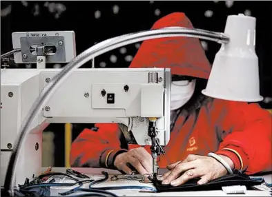  ?? STACEY WESCOTT/CHICAGO TRIBUNE ?? A worker wearing a mask and hood makes PPE masks at the Hart Shaffner Marx factory in April in Des Plaines.