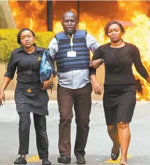  ?? AP-Yonhap ?? Security forces help civilians flee the scene as cars burn behind, at a hotel complex in Nairobi, Kenya, Tuesday. At least 15 people were killed when an Islamist suicide bomber and gunmen stormed an upmarket hotel and office complex.