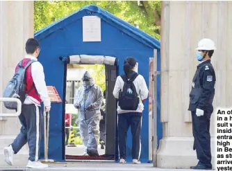  ?? AFP ?? An official in a hazmat suit waits inside the entrance of a high school in Beijing as students arrive yesterday.