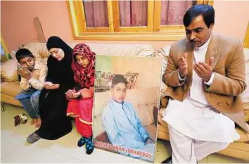  ?? AFP ?? Prayers for the victim The parents and siblings of slain Asfand Khan, a pupil who was killed during an attack by Taliban militants at an army-run school, pray alongside his photograph at their residence in Peshawar yesterday after the four men linked...