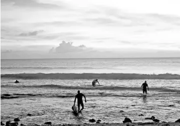  ??  ?? Goncalves, a surfer and hotel owner from the Portuguese town of Peniche, surfs off the coast of Kiritimati Island. Above right, surfers walk out of the water at sunset after surfing along the coast of Kiritimati Island, part of the Pacific Island...