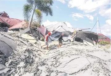  ?? — Reuters photo ?? Men walk on damaged road at Petobo sub-district following an earthquake in Palu, Central Sulawesi, Indonesia.