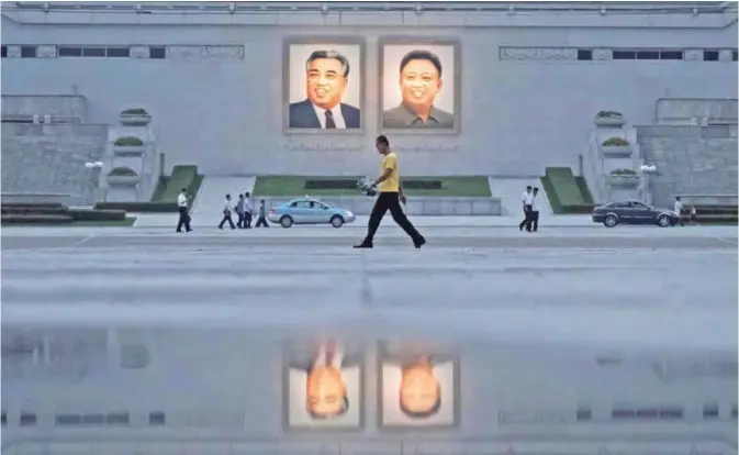  ??  ?? PYONGYANG: In a photo taken on July 21, 2017 pedestrian­s and vehicles pass before the portraits of late North Korean leaders Kim Il-Sung (left) and Kim Jong-Il (right). — AFP