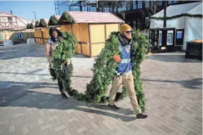  ?? MIKE DE SISTI / MILWAUKEE JOURNAL SENTINEL ?? Kenneth McFadden (left) and Eric Allison, with Criterion Production­s, carry garland to decorate a beer tent Wednesday as they help set up the Christmas market to be held on the plaza in front of Fiserv Forum in Milwaukee. Christkind­lmarket, a free "authentic German holiday festival," will be open Saturday through Dec. 31.