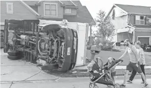  ?? NATI HARNIK, AP ?? Vincent and Lindsey Mercado and their children walk past an overturned truck and weatherdam­aged homes in the Hyda Hills neighborho­od of Bellevue, Neb., on Saturday, after a severe weather front passed through the previous evening.