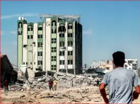  ?? — AFP ?? People walk past the ravaged building of Al Salam hospital, and at right, a partially-collapsed building in Khan Younis on Sunday.