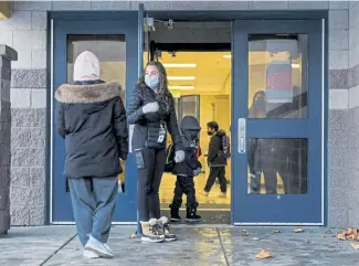  ?? Leah Hogsten, The Salt Lake Tribune via The Associated Press ?? Teaching assistant Becca Stevens holds the door open for returning Escalante Elementary students in Salt Lake City, Utah, on Monday. Salt Lake City School District reopened all of the district’s elementary schools to in-person learning on Monday.