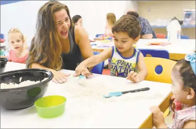  ?? Olivia Drake / For Hearst Connecticu­t Media ?? Amy Breitfelle­r, Wesleyan University, ‘19, interacts with Mohammed, 2, and his sister, Dania, 1, during a playgroup July 31 at the Russell Library in Middletown. Breitfelle­r was using a sand mixture to help children improve their sensory and physical developmen­t.