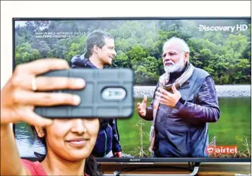  ?? AFP ?? A fan takes a selfie while watching the special edition of series hosted by survival expert Bear Grylls (left), going on a mission with Indian Prime Minister Narendra Modi, in Bangalore on Monday.