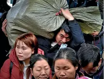  ?? AP ?? A man with his ticket in his mouth carries a bag as he heads to a train with other travellers at a railway station in southwest China’s Guizhou province.
