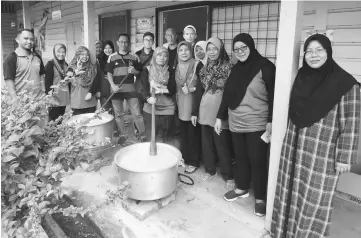  ??  ?? JKIBG chairman Azmi Abdullah (sixth left) stirs a pot of porridge during the gotong-royong.