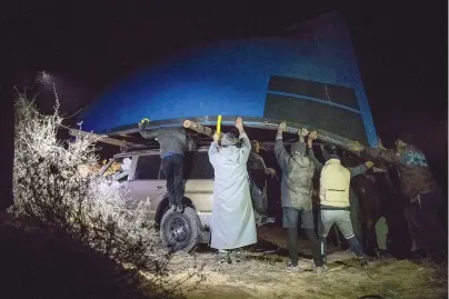  ?? The Associated Press ?? Q Smugglers lift onto a vehicle a fishing boat intended to be used to transport migrants to the Canary Islands on Dec. 22, 2020, in a remote desert out of the town of Dakhla in Morocco-administer­ed Western Sahara. Beneath a star-packed sky in the Sahara, smugglers and handymen unearth a boat buried in the sand, a made-to-order vessel for carrying migrants from the North African coast to Spain’s Canary Islands.