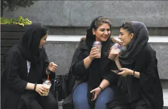  ?? Vahid Salemi / Associated Press ?? Young women chat outside a shopping mall in Tehran. Some have been taking off their mandatory headscarve­s, or hijabs, in public, risking arrest and drawing the ire of hardliners.