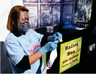  ?? — AFP ?? A volunteer woman gets a roll of “I Voted” stickers ready next to a ballot box for dropping off mail-in ballots on the first day of inperson early voting on Saturday in Las Vegas, Nevada.